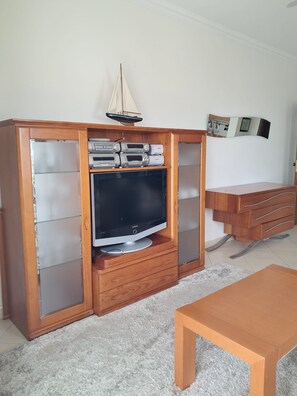 Ein Wohnzimmer mit einer Holz-Unterhaltungsecke, einem Flachbildfernseher, einer kleinen Segelboot-Dekoration, einem Spiegel und einem Holztisch.