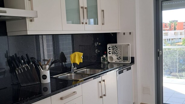 Una cocina moderna con armarios blancos, encimera negra y un lavamanos visible.