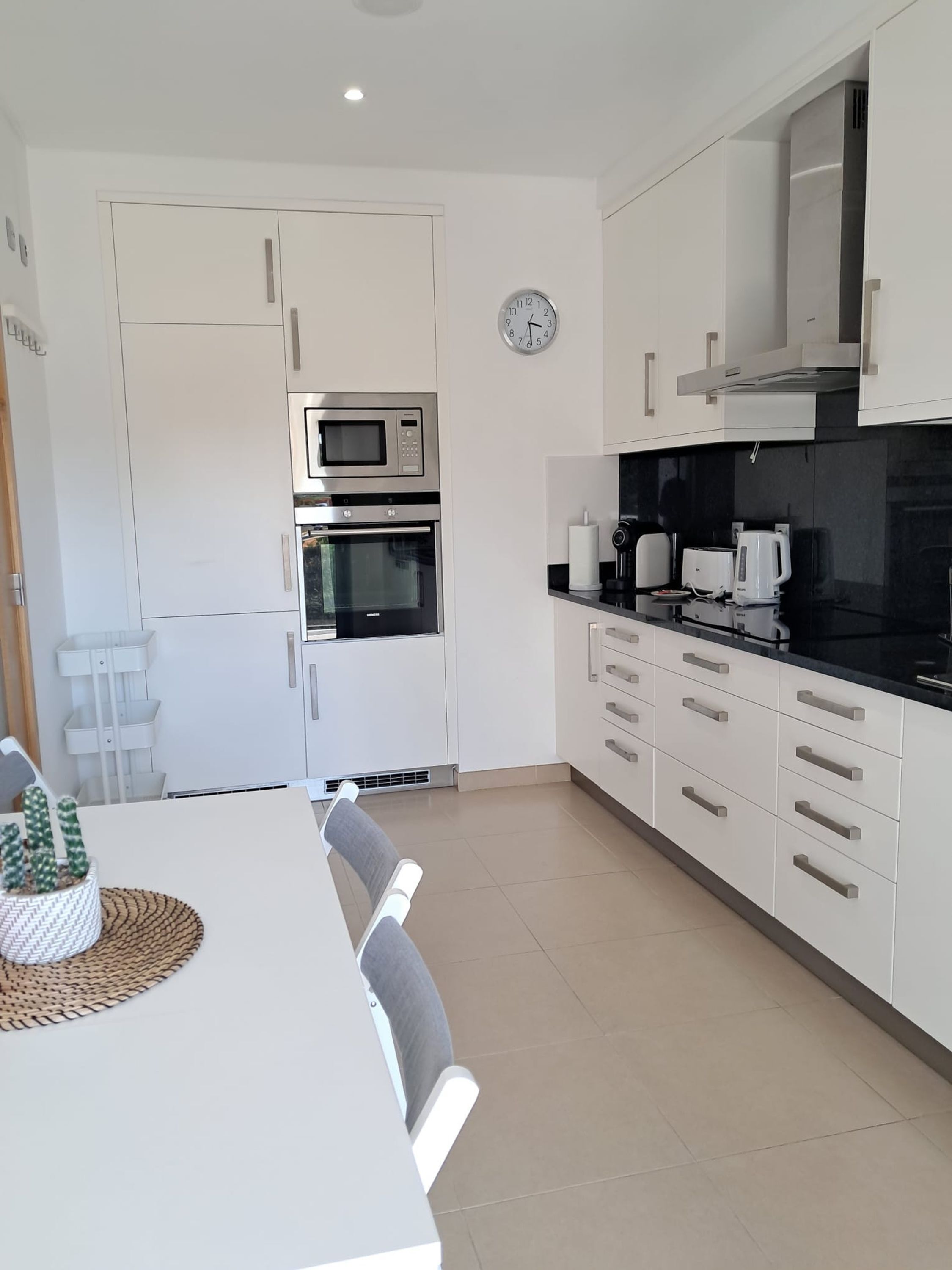 A modern kitchen with white cabinetry, a microwave, oven, and a clock on the wall.