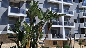 Un edificio de varios pisos con balcones, fachada de piedra y plantas tropicales.
