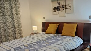 Un dormitorio con cama, mesita de noche, lámpara, ventana con cortinas y decoración en la pared.