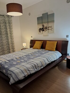 Ein Schlafzimmer mit einem großen Bett, einem Nachttisch, einer Lampe und einem an der Wand hängenden Kunstwerk.