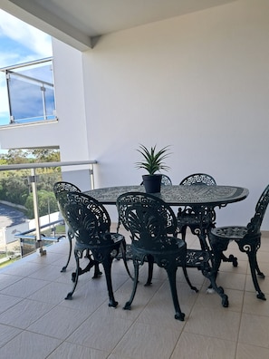 Un balcon avec une table ronde et des chaises, un pot de fleurs et une vue sur une étendue d’eau.