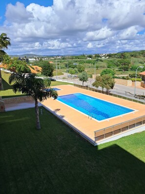 Ein rechteckiger Swimmingpool mit glasklar blauem Wasser, umgeben von einer Sandbadeplattform und begrenzt durch eine niedrige Steinmauer.