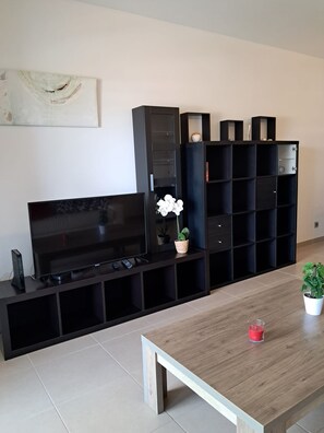 Ein modernes Wohnzimmer mit Flachbildfernseher, schwarzen Regaleinheiten, einem Holztisch und einer Topfpflanze.