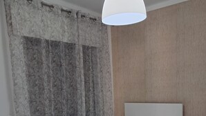 Een slaapkamer met een bed, nachtkastje, lamp en gordijnen.