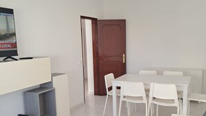 Een moderne woonkamer met een bank, een eettafel met stoelen, een televisie op een standaard en een houten deur.