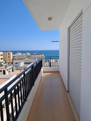 A balcony with a view of the sea, a tiled floor, and a white wall with a shutter. - T2 Vista MAR in Quarteira (Faro)