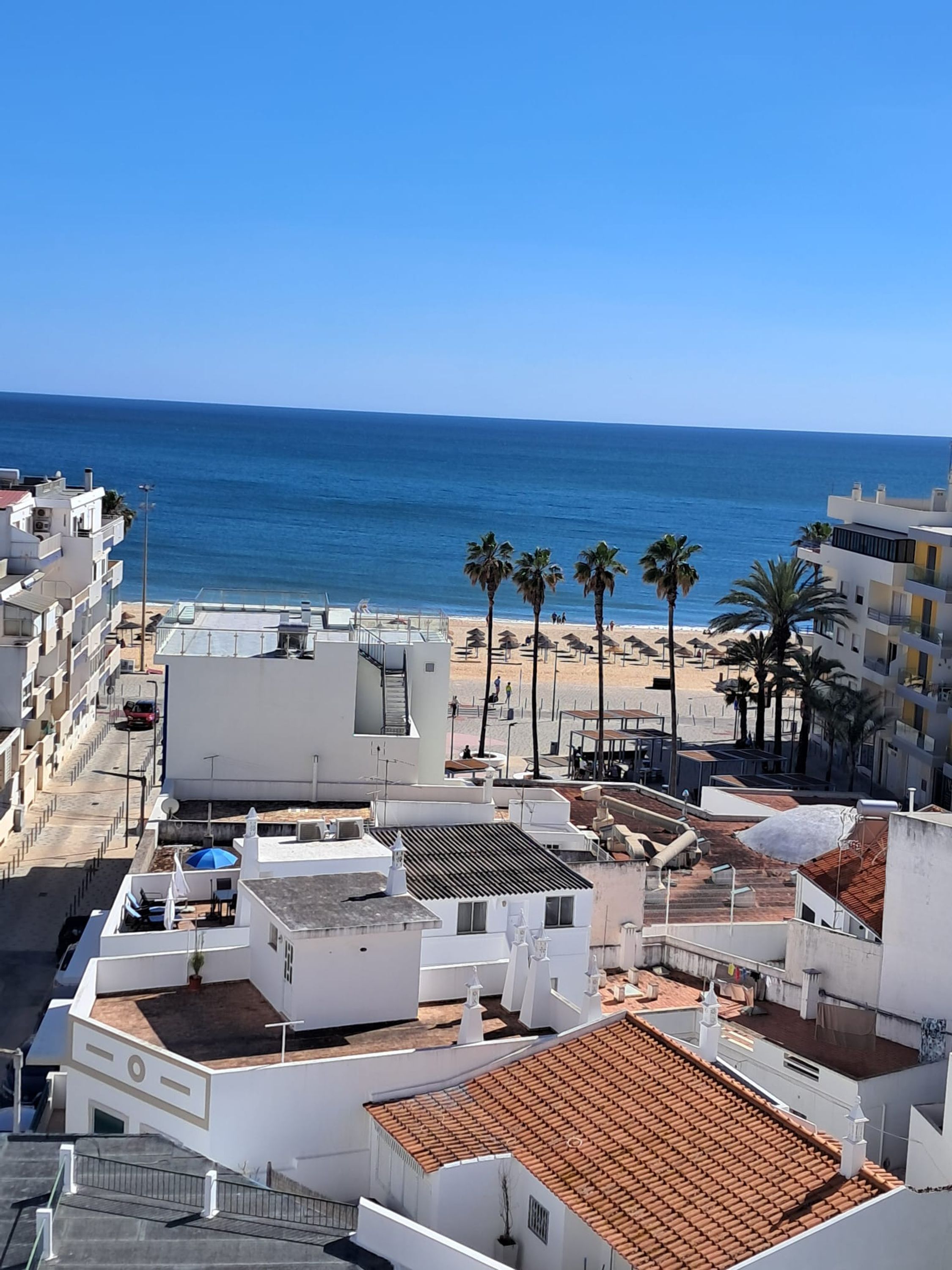 A coastal building complex with multiple white structures, a rooftop terrace, and a view of the beach and ocean.