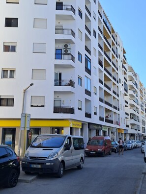A multi-story residential building with balconies, a street in front, and parked cars. - T2 Vista MAR in Quarteira (Faro)