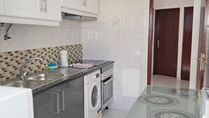 Een keuken met witte kastjes, een wasmachine, een magnetron en een tafel met glazen blad.