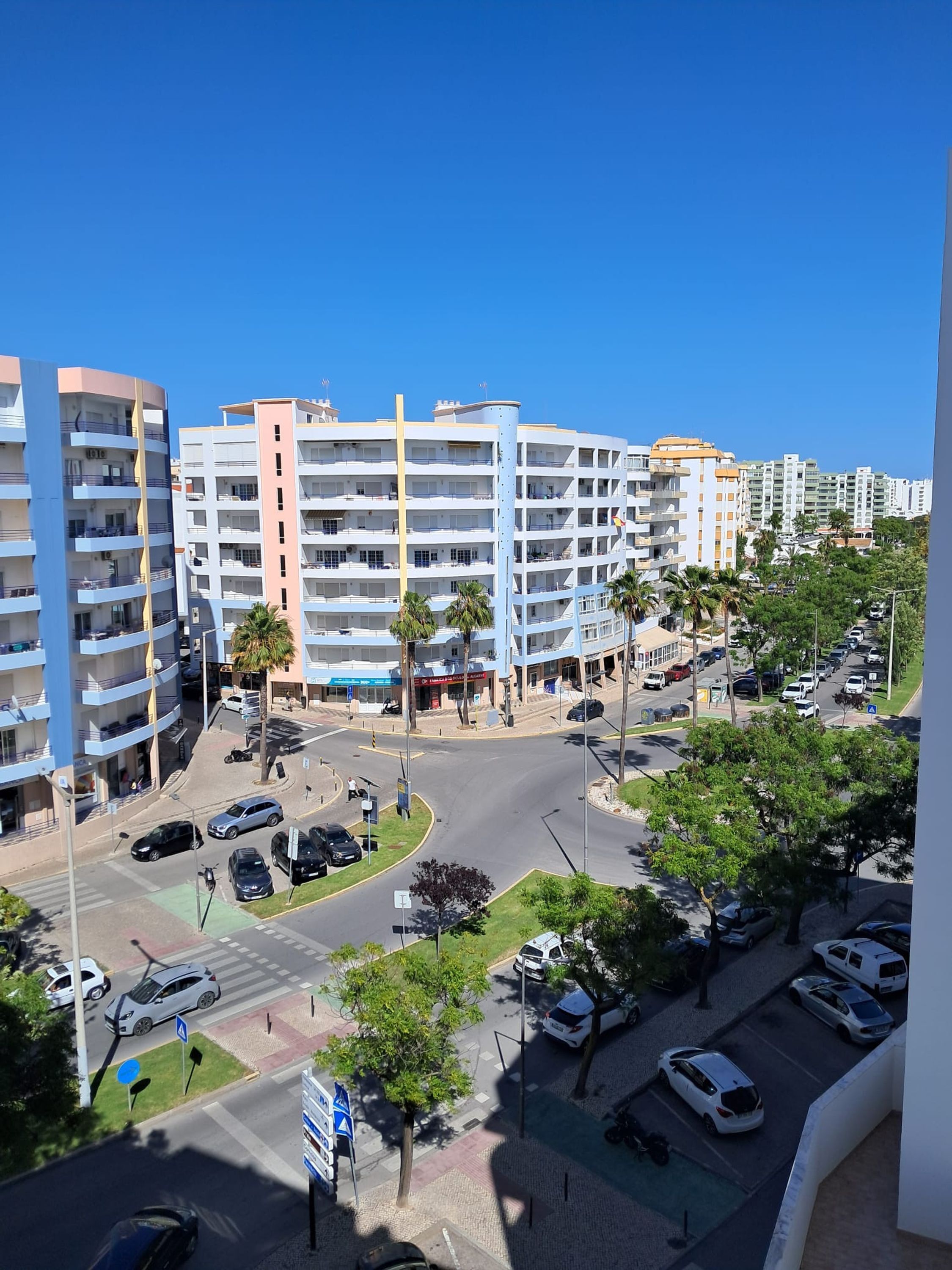 A multi-story residential building with balconies, a parking lot, and a clear blue sky.