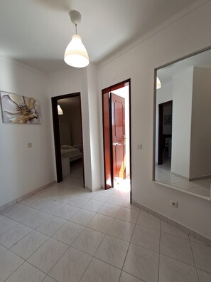 A spacious room with a tiled floor, a ceiling light, a door leading to another room, and a wall-mounted mirror. - T2 Vista MAR in Quarteira (Faro)