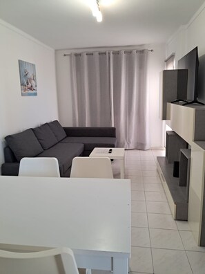 A modern living room with a sofa, a coffee table, a TV on a stand, and a painting on the wall. - T2 Vista MAR in Quarteira (Faro)