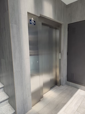 A modern elevator with a warning sign, a staircase, and a plain door. - T2 Alto Forte A C Garagem (Loulé)