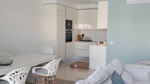 Un salon moderne avec un canapé blanc, une table à manger avec des chaises et un coin cuisine équipé de meubles et d’appareils électroménagers.