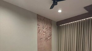 Quarto moderno com uma cama grande, mesa de cabeceira, cadeira, ventilador de teto e janela com cortinas.