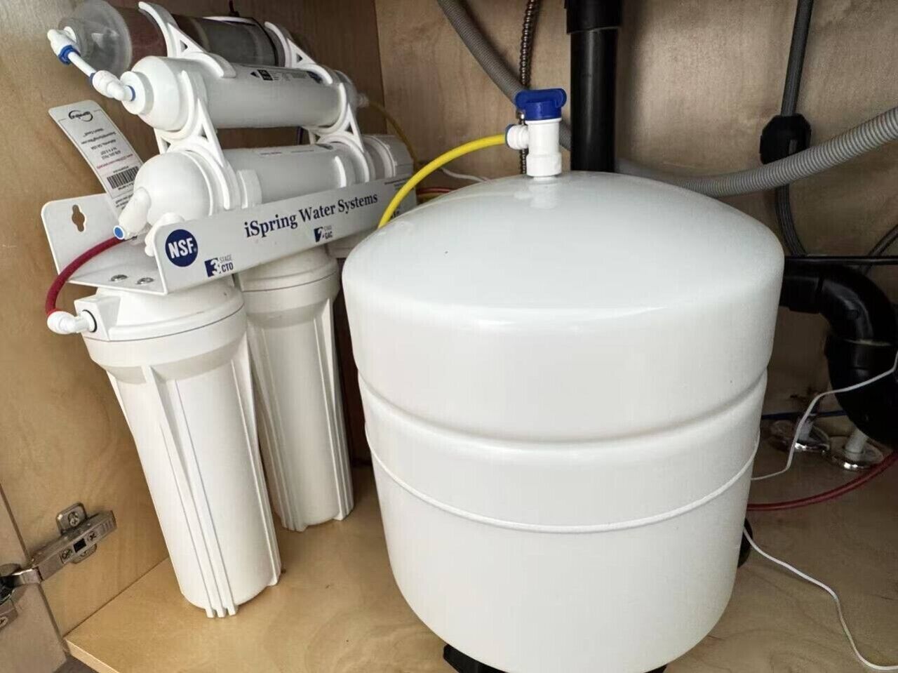 A water filtration system with a large white tank and two smaller tanks, connected by hoses.