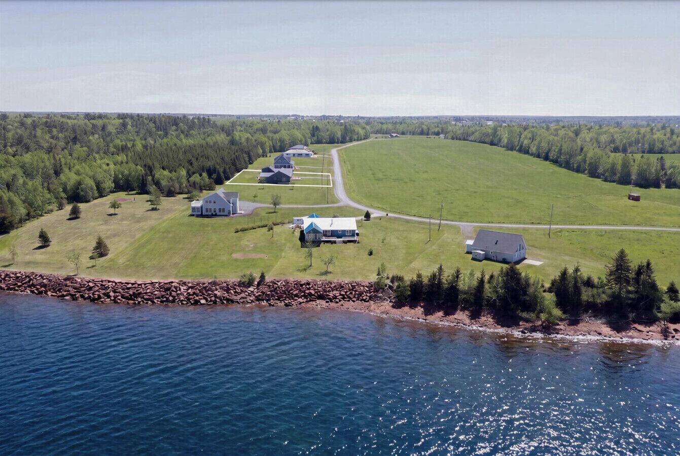 A coastal property with a main house, several smaller buildings, and a large green field.