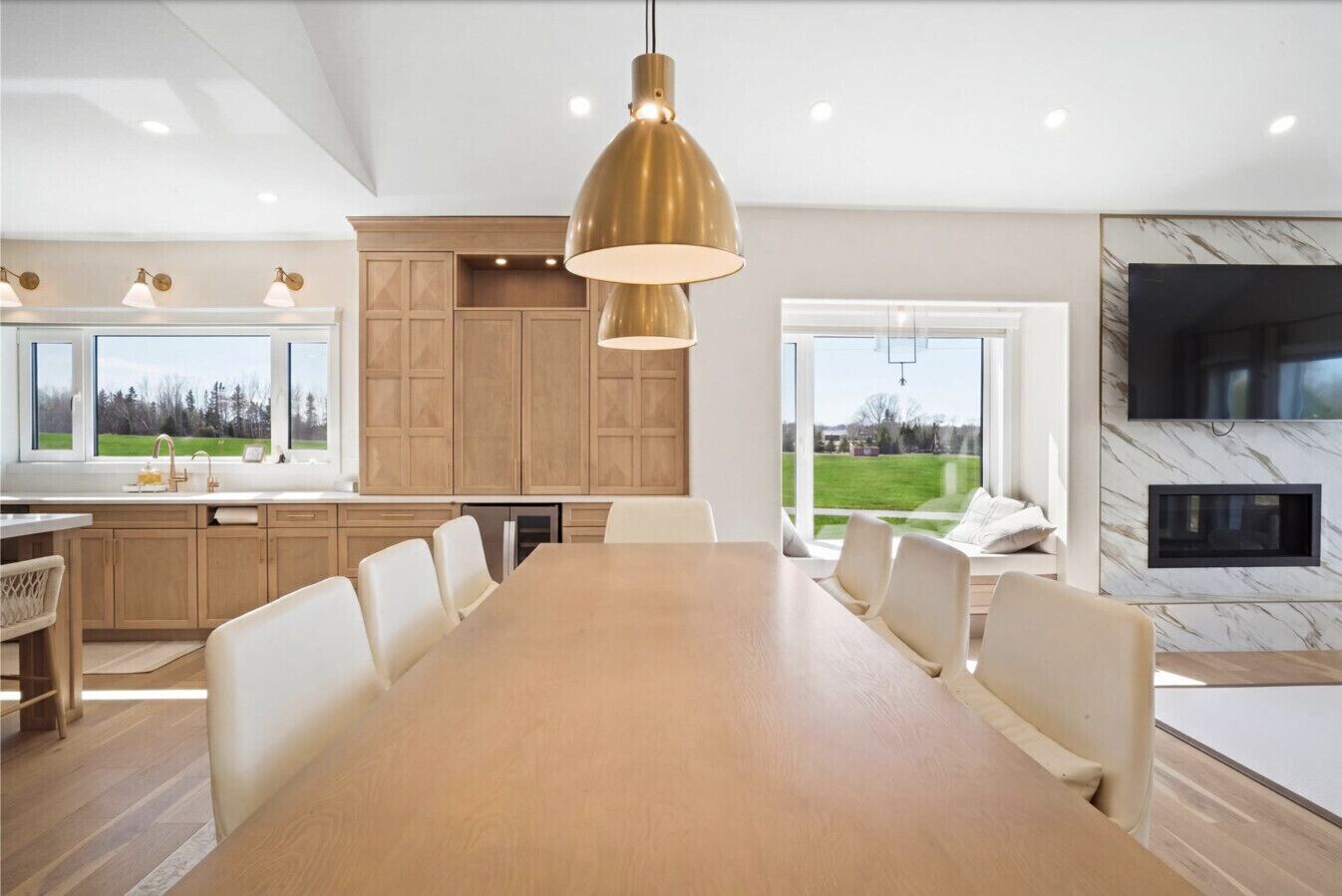 Een moderne keuken met houten kastjes, een grote eettafel en uitzicht op een groen landschap.