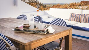 A wooden table with a tray, a glass pitcher, and a mug, set on a terrace with a white sofa and patterned cushions. - Al Porta Townhouse by Cadenzalux (Beja)