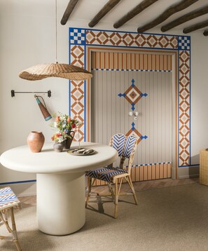 Une pièce avec une table ronde, une chaise en osier, un vase de fleurs et un mur orné de motifs.