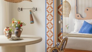 A room with a bed, a wicker chair, a small table with a vase of flowers, and a hanging light fixture. - Al Porta Townhouse by Cadenzalux (Beja)