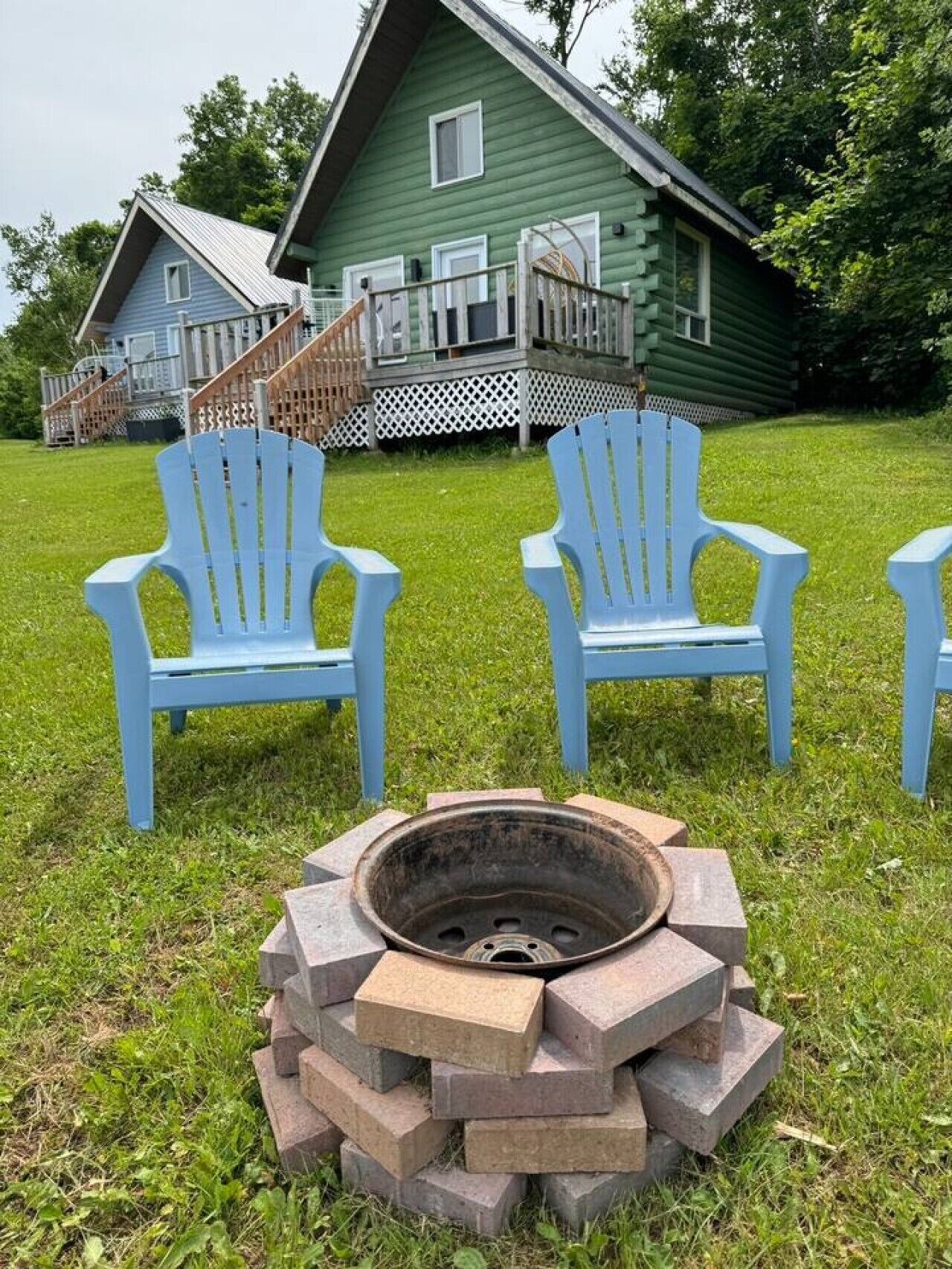 Ett grönt hus med en veranda, två blå Adirondack-stolar och en eldstad av sten.
