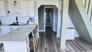 A kitchen with a central island, wooden chairs, and a view into the dining area. - Serene Cove Retreat Green Cottage-overseeing beautiful Montague River and and peaceful harbor (Montague)
