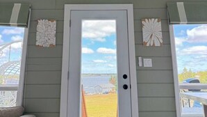 A room with a white door, a small window, and a view of a field. - Serene Cove Retreat Green Cottage-overseeing beautiful Montague River and and peaceful harbor (Montague)