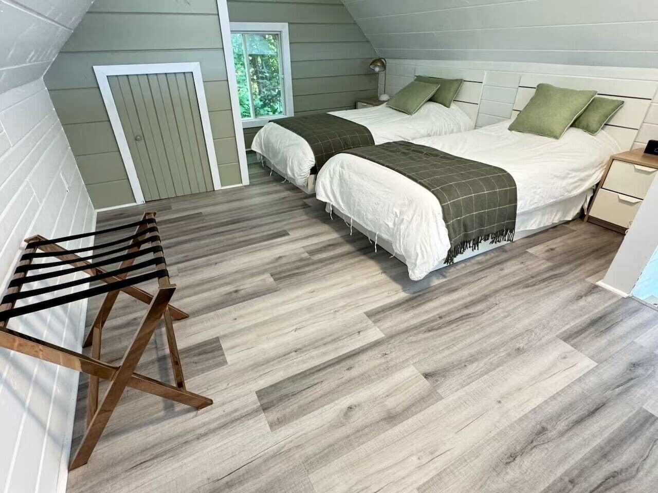 Een kamer met twee bedden, een houten wasrek en een raam met uitzicht op groen.
