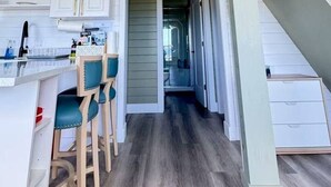 A kitchen with white cabinets, a bar area with stools, and a staircase leading to an upper level. - Serene Cove Retreat Green Cottage-overseeing beautiful Montague River and and peaceful harbor (Montague)