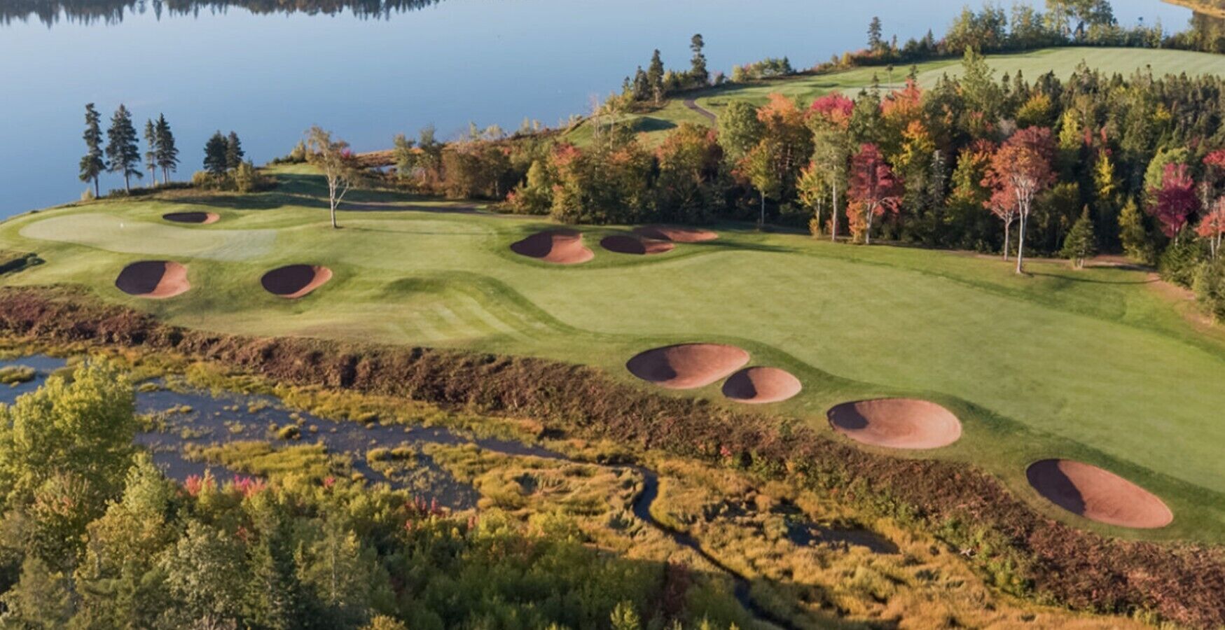 Un parcours de golf avec des bunkers, un lac et un paysage aux couleurs automnales.