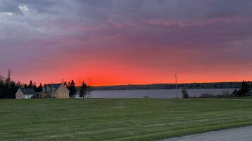 A rural landscape with a house, open fields, and a body of water during sunset.