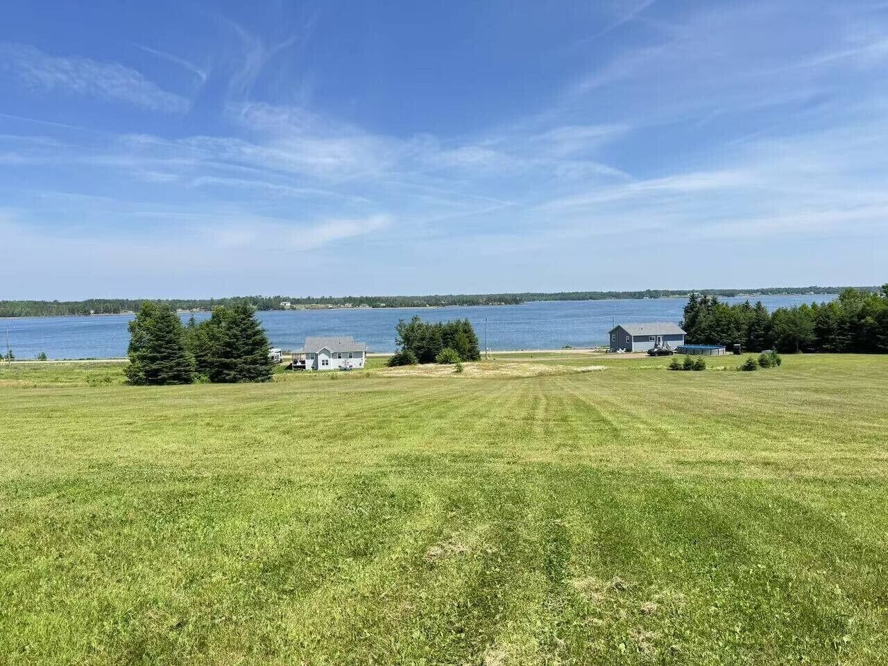 A grassy field with a small house and a body of water in the background.