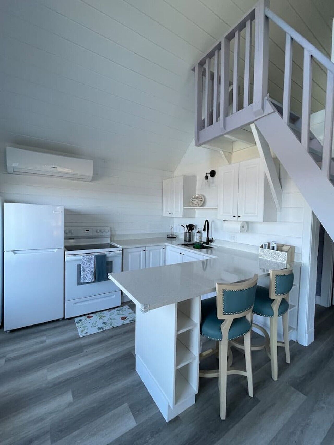 Une cuisine avec des meubles blancs, un réfrigérateur blanc, une cuisinière et un coin repas avec deux chaises.