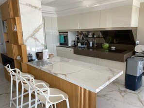 Een moderne keuken met een marmeren aanrechtblad, inbouwapparatuur en een zithoek met witte stoelen.