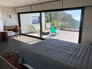Een slaapkamer met een groot bed, een bureau en een stoel, een balkon met uitzicht op een berg en een zwembad.