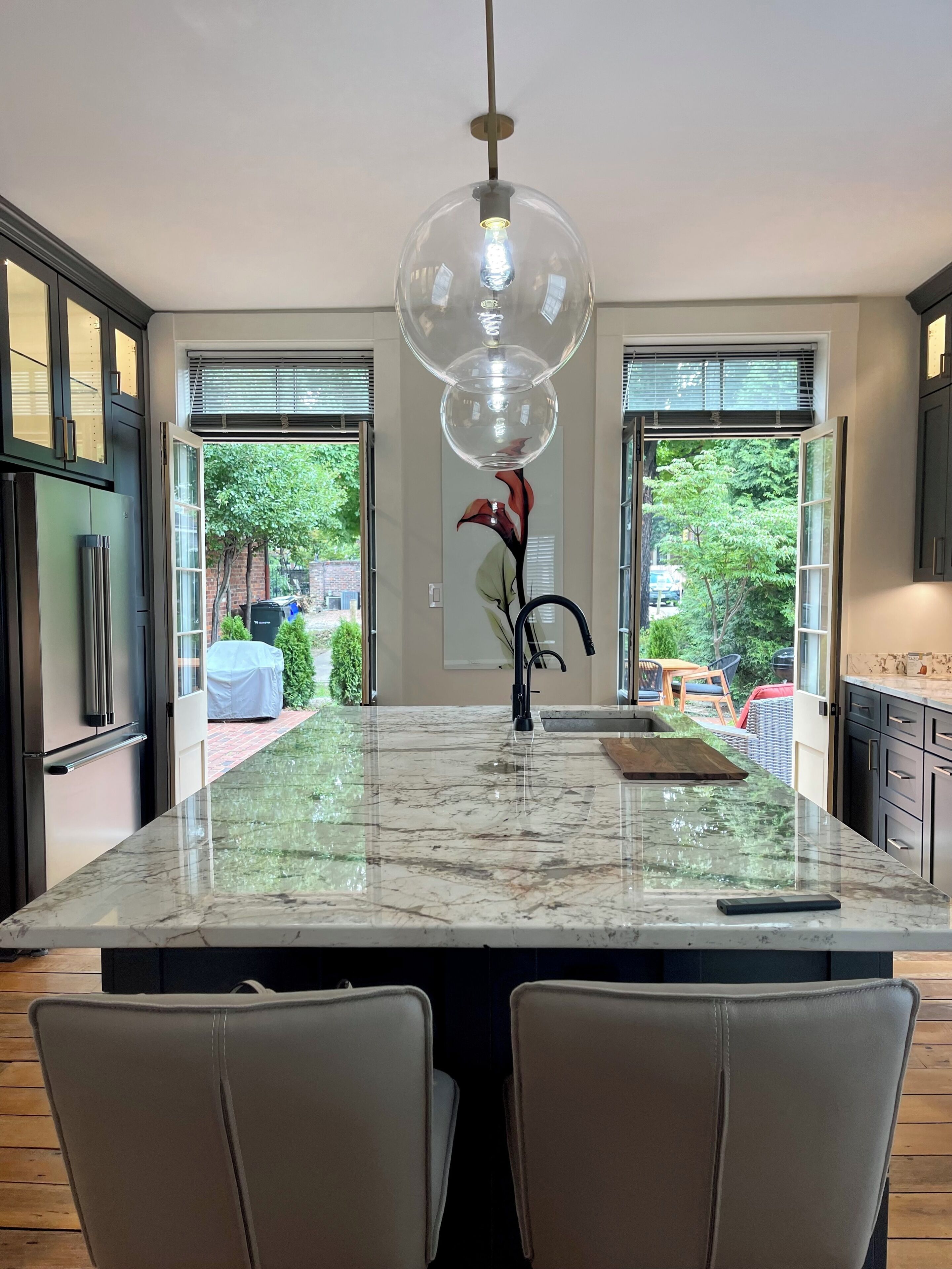 A modern kitchen with a large island, black cabinets, and a view of the outdoors.