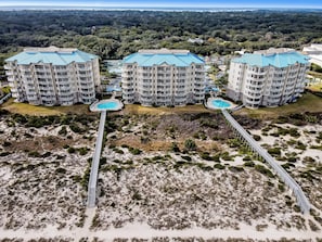 A high-rise hotel with multiple balconies, a central swimming pool, and a beach access walkway.