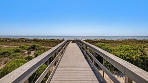 Une promenade en bois menant à une plage, sous un ciel dégagé.