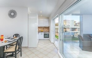 Eine moderne Küche mit weißen Schränken, ein Essbereich mit Tisch und Stühlen sowie eine große Glasschiebetür, die auf einen Balkon mit Gartenmöbeln führt.