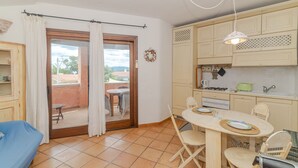 Et værelse med spisebord, stole, sofa, et tekøkken og en skydedør til en udendørs terrasse.