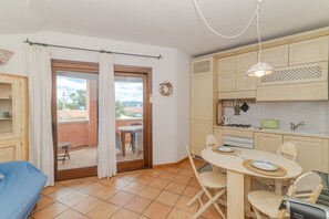 Ein Zimmer mit Esstisch, Stühlen, einer Couch, einer Küchenzeile und einer Glastür zum Außenbereich.