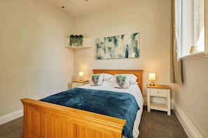 Une chambre à coucher avec un lit en bois, deux tables de chevet avec des lampes, une plante fixée au mur et un grand tableau abstrait.