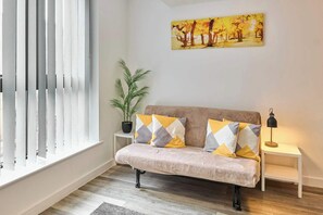 A living room with a sofa, cushions, a plant, a painting, and a lamp. - Host & Stay | Flat 3, 4 Leigh Street (Liverpool)