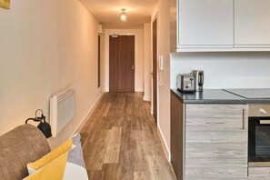 A hallway with a wooden floor, a door at the end, and a kitchenette with a toaster and kettle. - Host & Stay | Flat 3, 4 Leigh Street (Liverpool)