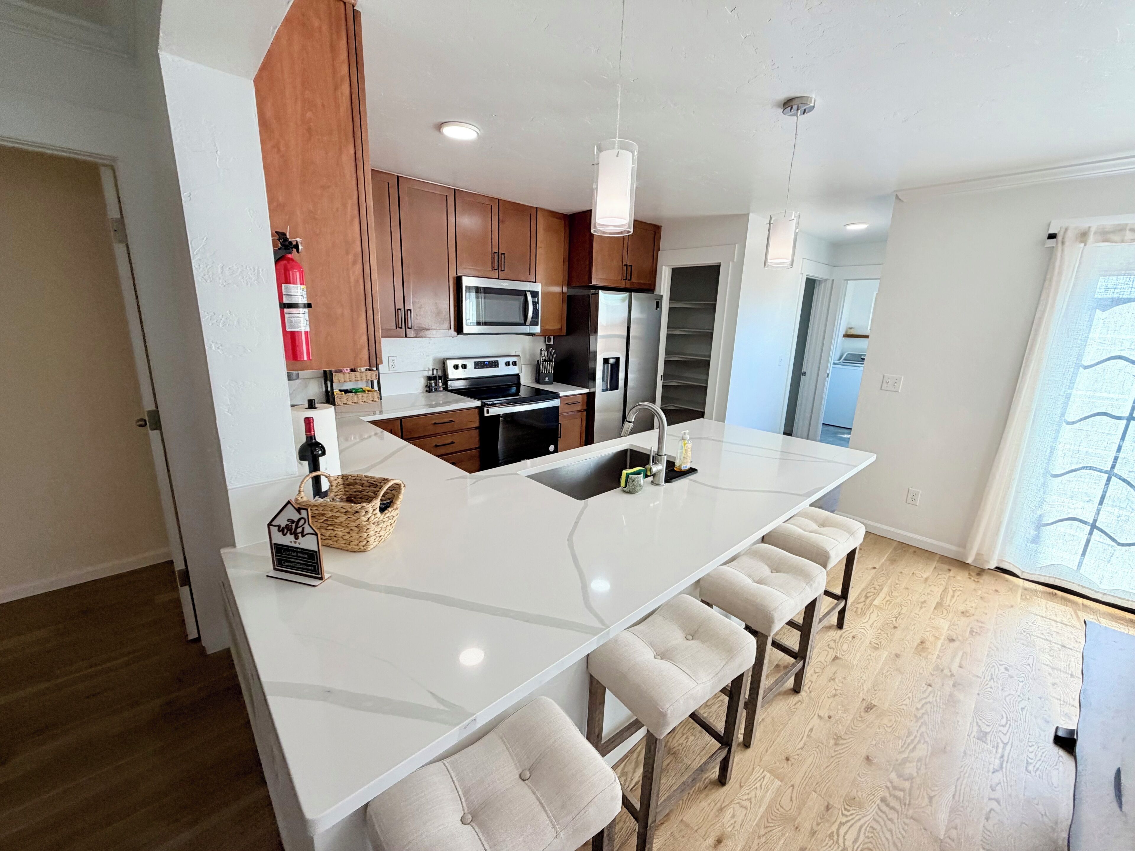 A modern kitchen with a central island, wooden cabinets, stainless steel appliances, and a large window.