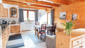 A wooden cabin interior with a kitchen, dining area, and a sofa.