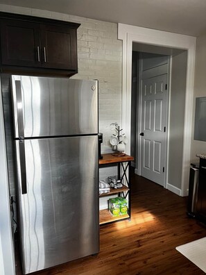 Una cocina con un refrigerador de acero inoxidable, estantes de madera y una pared de ladrillo blanco.